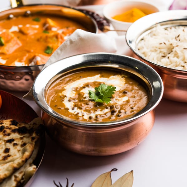 Indian dishes in copper bowls, including dal makhani, paneer butter masala, rice, and naan.