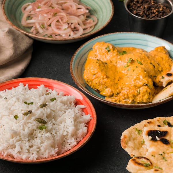 Indian butter chicken, rice, naan bread, pickled onions, and spices on a dark surface.