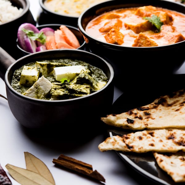 A vibrant spread of Indian dishes including palak paneer, butter chicken, rice, naan, and spices.