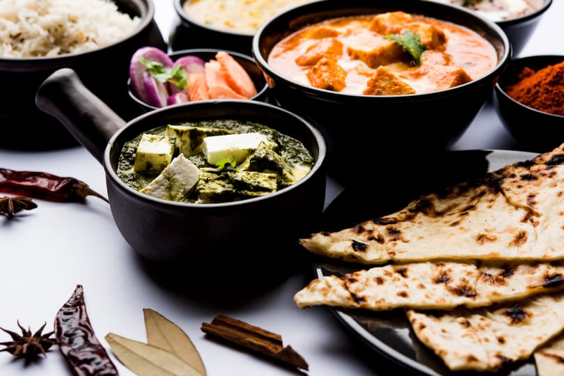 A vibrant spread of Indian dishes including palak paneer, butter chicken, rice, naan, and spices.